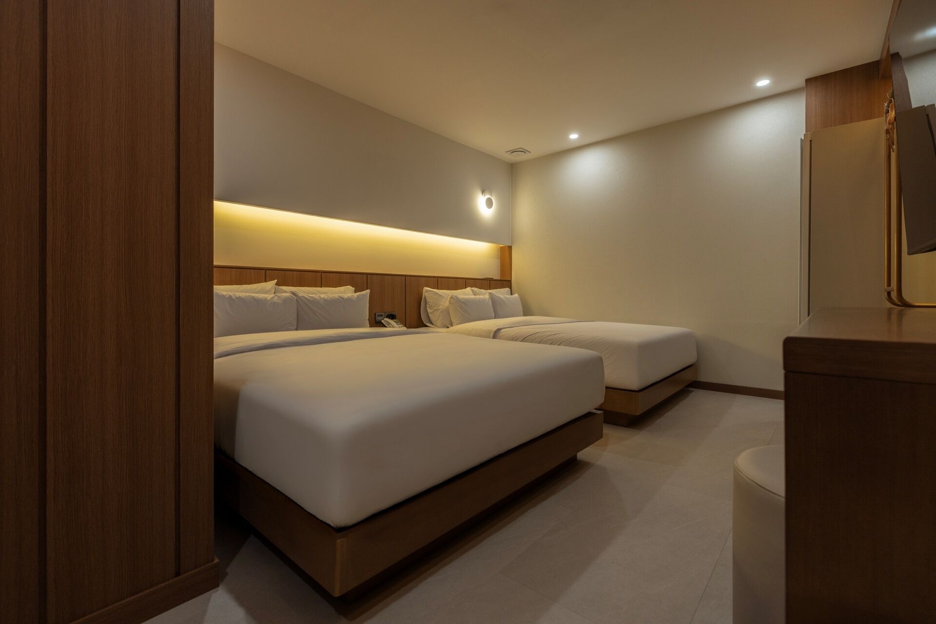 Habitación de hotel con dos camas, una mesita de noche, un espejo y ducha integrada.