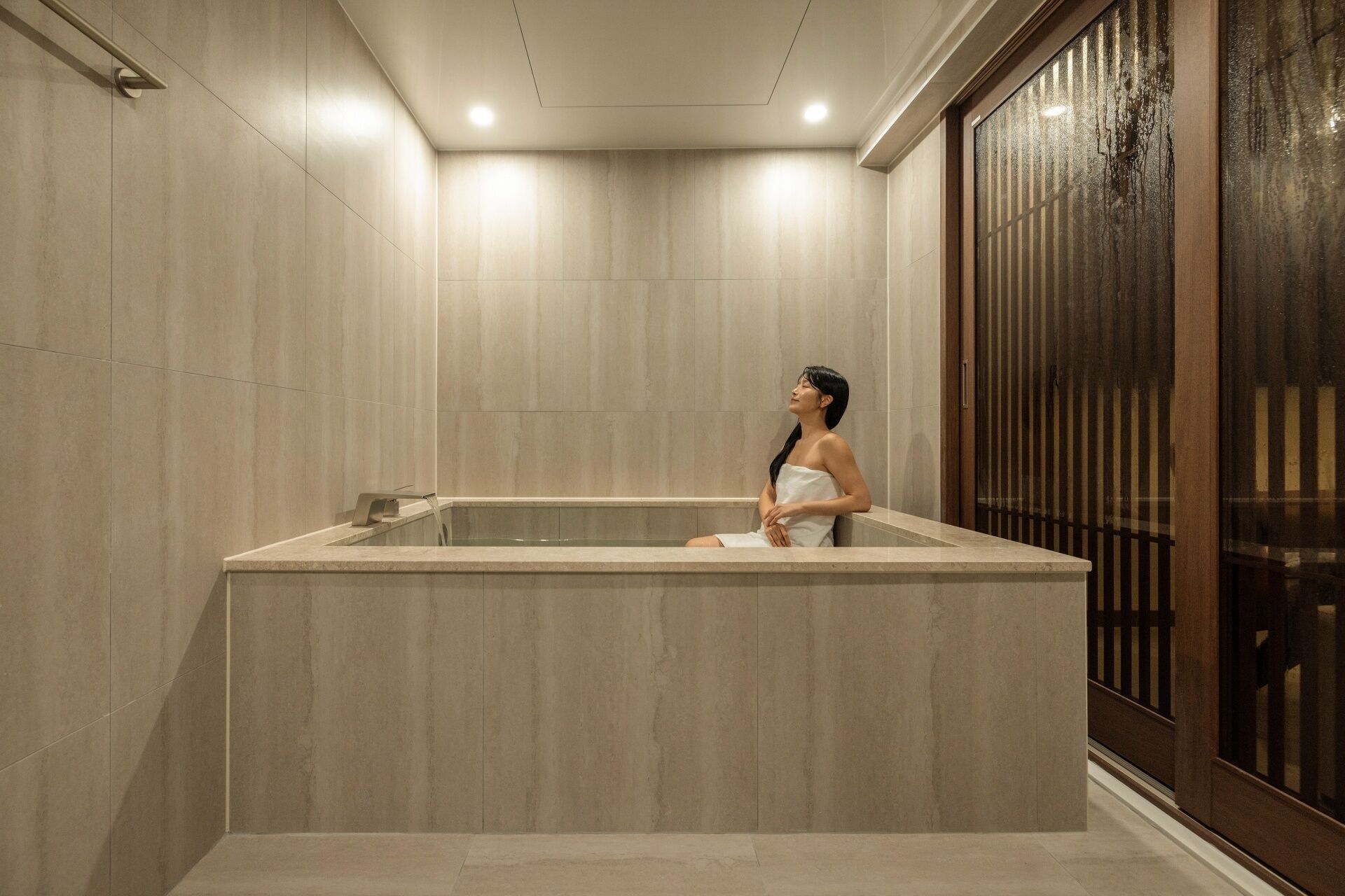 A spa area with a large bathtub, a wooden door with vertical slats, and a tiled wall.