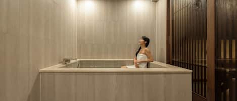 Un área de spa con una bañera grande, una puerta de madera con listones verticales y una pared de azulejos.