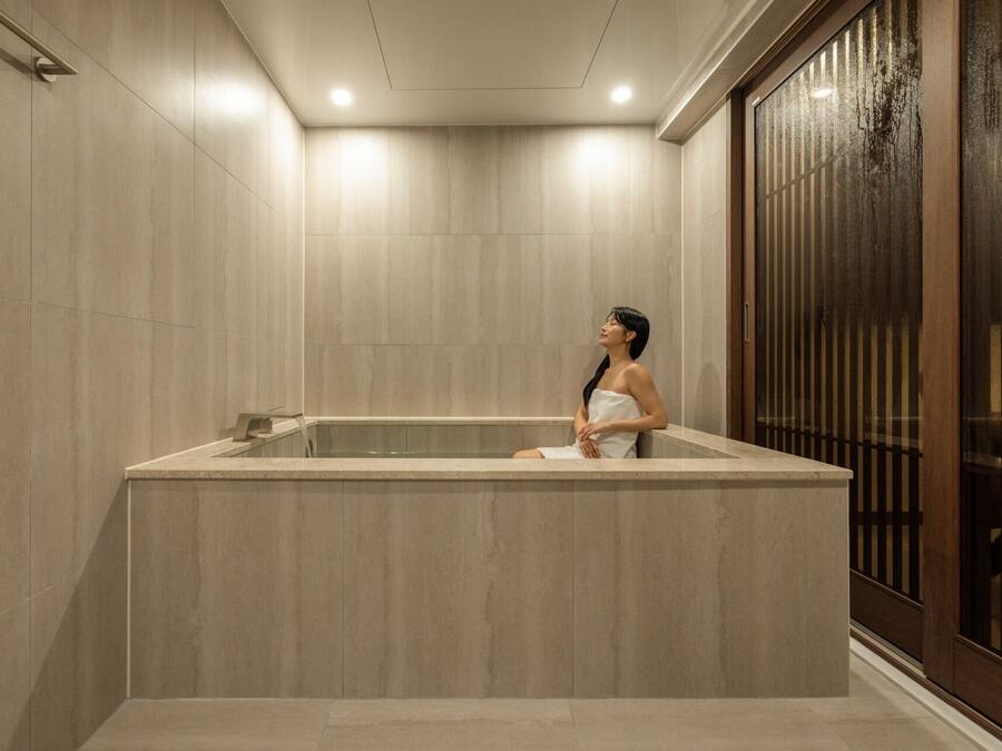 A spa area with a large bathtub, a wooden door with vertical slats, and a tiled wall.