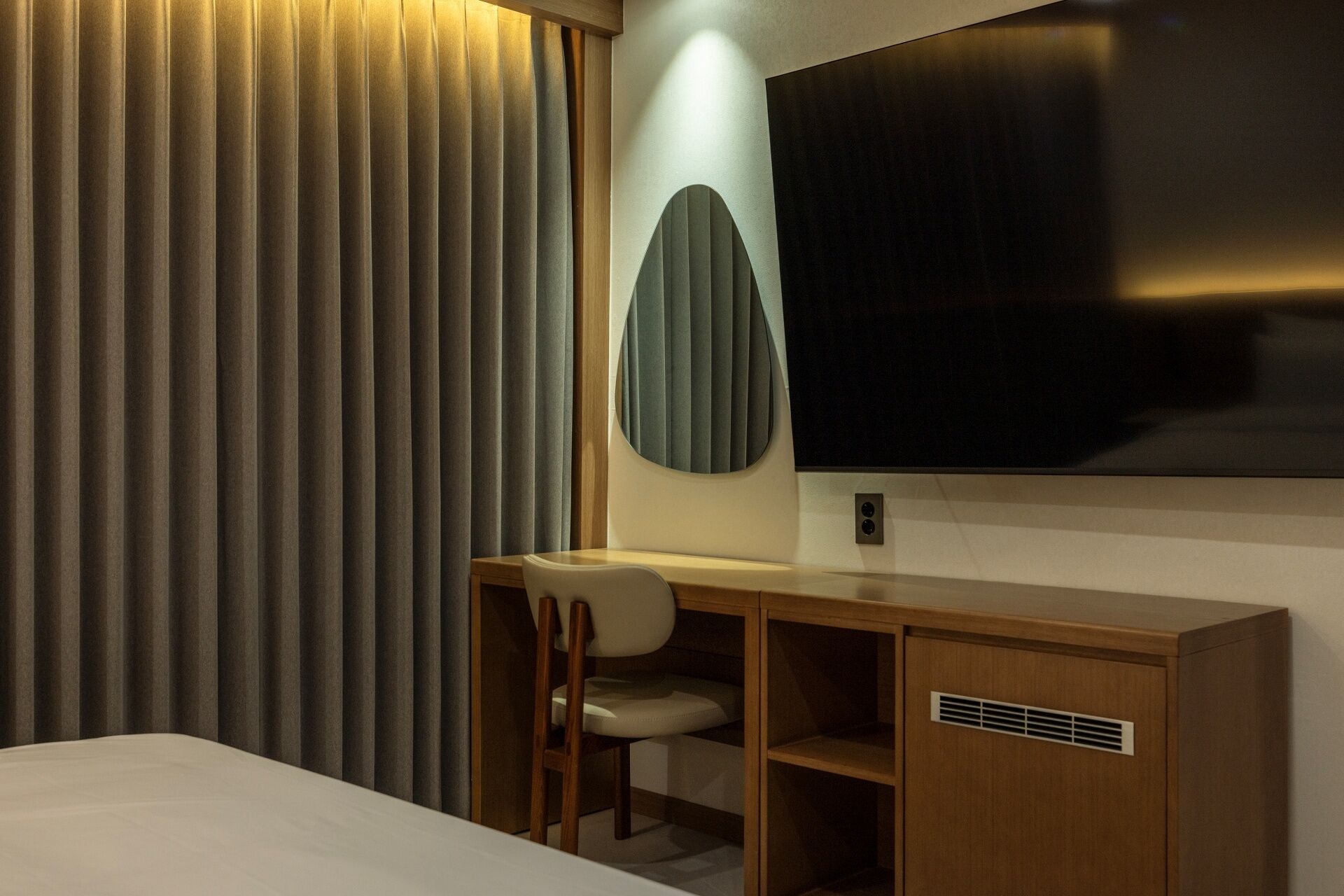 Habitación de hotel con cama, escritorio con silla, televisión y un amplio ventanal con persianas verticales.