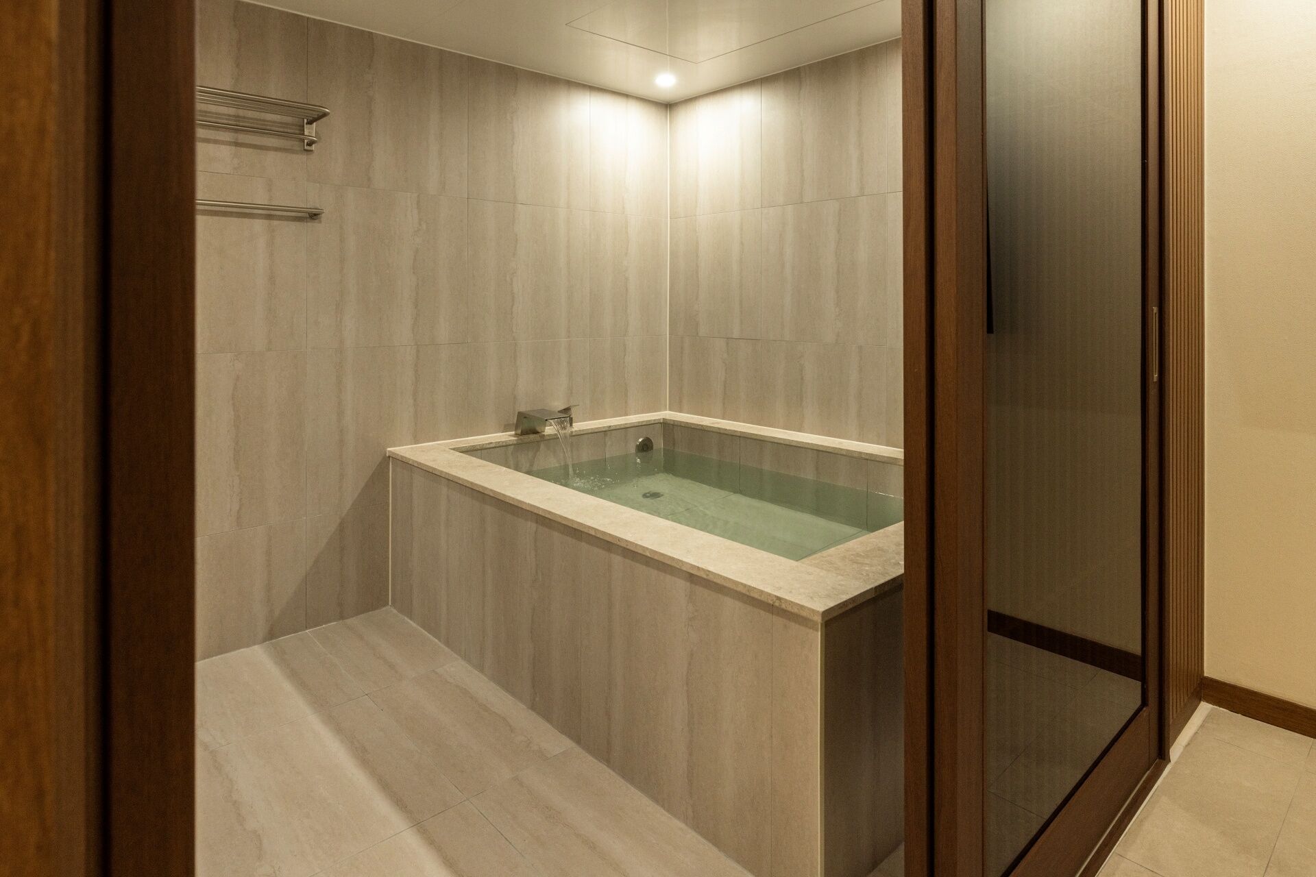 A modern bathroom with a glass-enclosed bathtub, wooden paneling, and a built-in shelf.