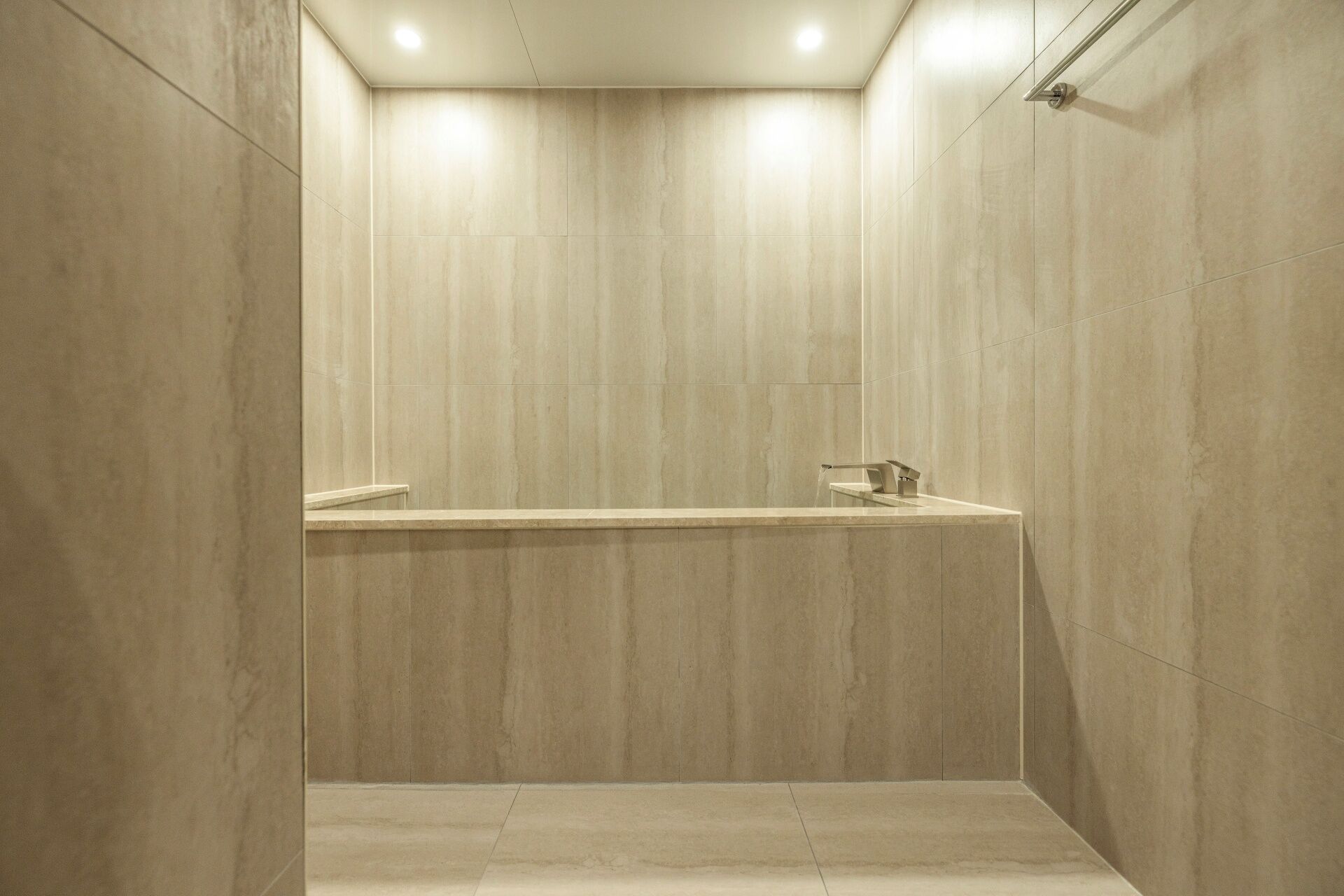 Een moderne douche met een minimalistisch ontwerp, met één kraan en een effen, lichtgekleurde vloer.