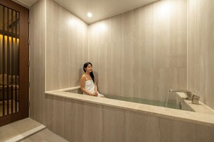Una persona en una bañera en una habitación con paredes de azulejos y una puerta de madera.