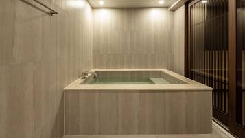 Un baño moderno con una bañera rectangular, paredes con azulejos y una puerta corredera de madera.