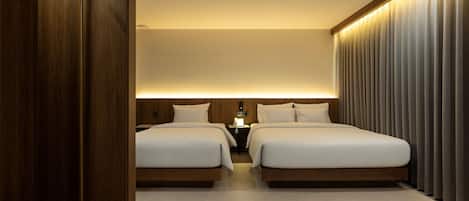 Habitación de hotel con dos camas, un armario de madera, una mesita de noche con lámpara y una ventana con cortinas.