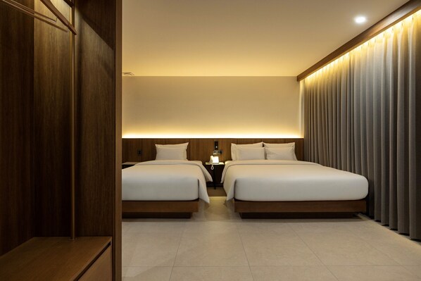A hotel room with two beds, a wooden wardrobe, a bedside table with a lamp, and a curtain-covered window.