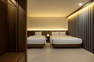 Habitación de hotel con dos camas, un armario de madera, una mesita de noche con lámpara y una ventana con cortinas.