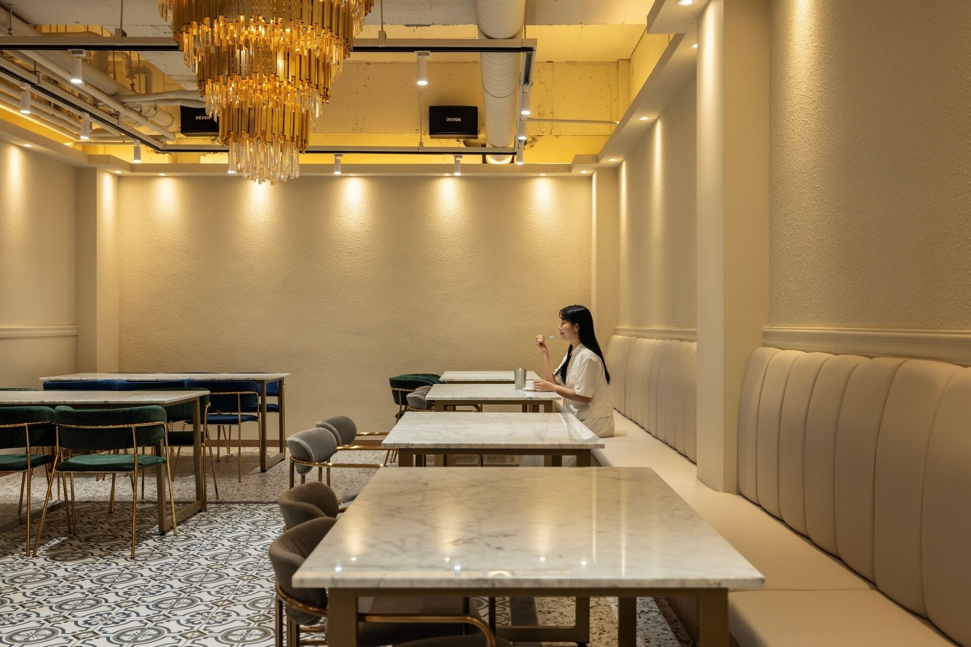 A hotel dining area with marble tables, green upholstered chairs, and a woman sitting at a table.