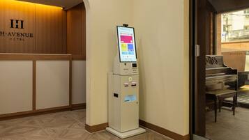 A hotel reception area with a digital kiosk, a piano, and a wooden wall with the hotel name.