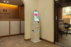 Zona de recepción de un hotel con un quiosco digital, un piano y una pared de madera que muestra el nombre del hotel.