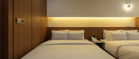 Una habitación de hotel con dos camas, una mesita de noche con teléfono y una lámpara fijada a la pared.