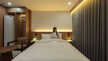 Una habitación de hotel con cama, mesita de noche, silla y teléfono en la pared.
