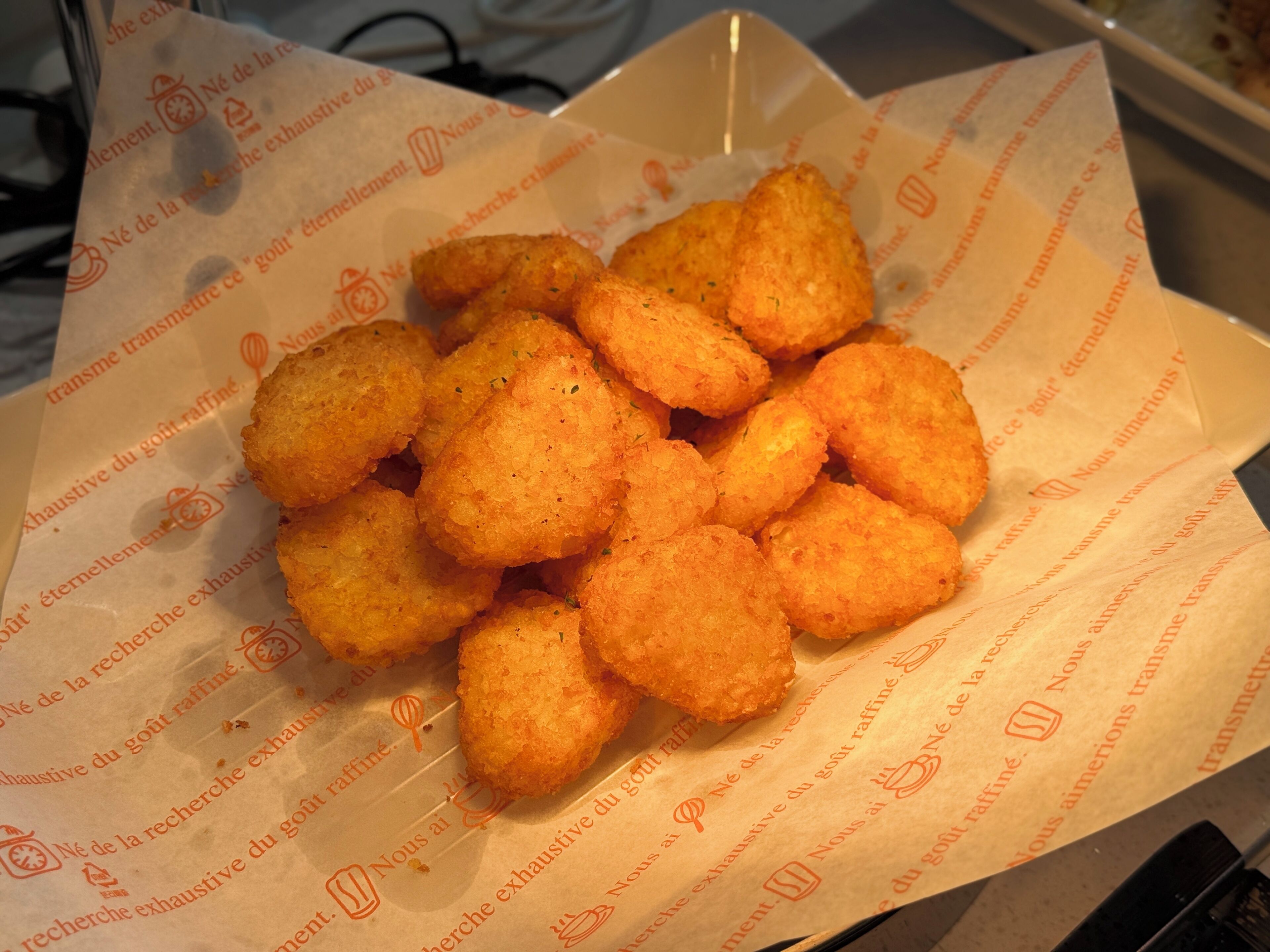 Une assiette de petites bouchées frites, dorées et croustillantes, posée sur une feuille de papier avec du texte.