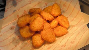 Une assiette de petites bouchées frites, dorées et croustillantes, posée sur une feuille de papier avec du texte.