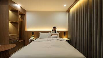 A hotel room with a bed, bedside tables, a wardrobe, and a curtain.