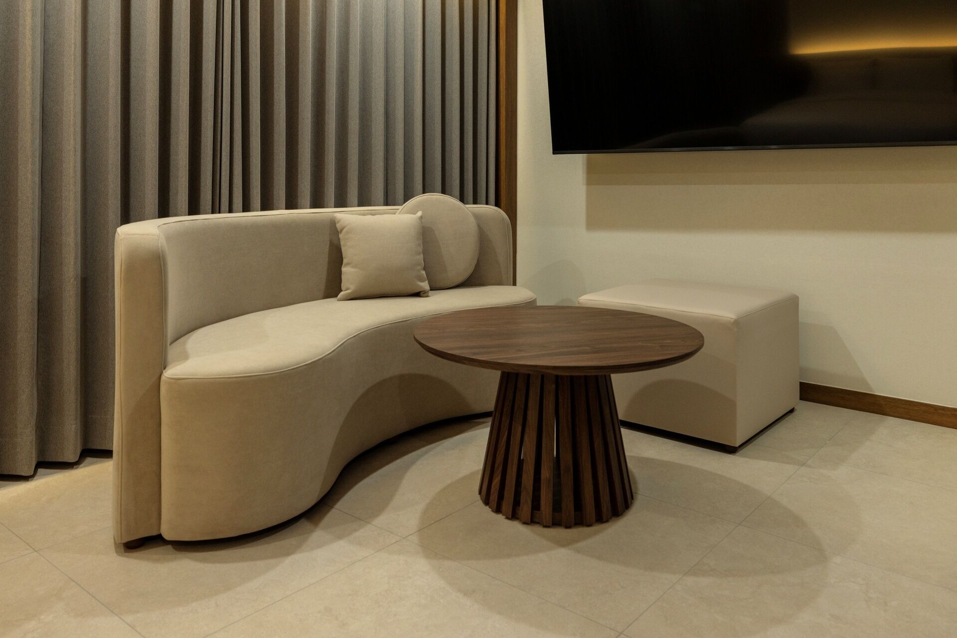 A modern living room with a curved sofa, a round wooden coffee table, and a flat-screen TV mounted on the wall.