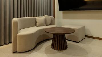 A modern living room with a curved sofa, a round wooden coffee table, and a flat-screen TV mounted on the wall.