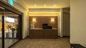 A hotel lobby with a reception desk, wooden cabinets, a coffee machine, and a microwave.