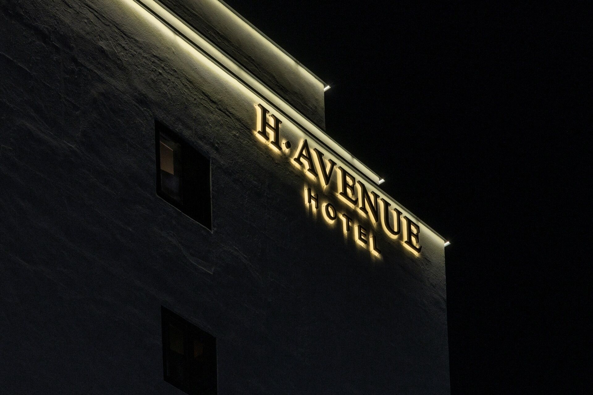 A building with a sign that reads 'H. AVENUE HOTEL' illuminated at night.