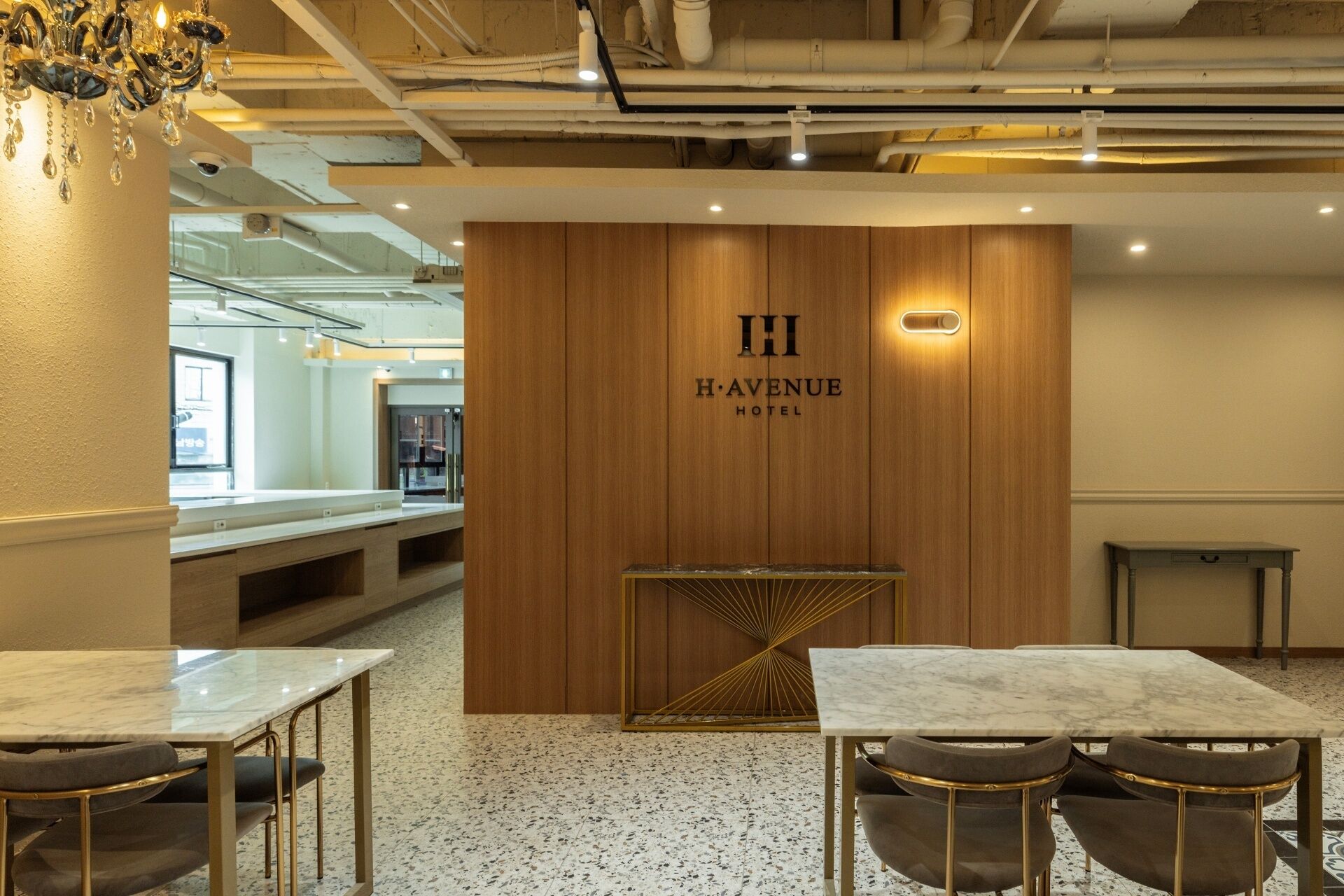A hotel lobby with a marble reception desk, a wooden wall with the hotel name, and a modern chandelier.