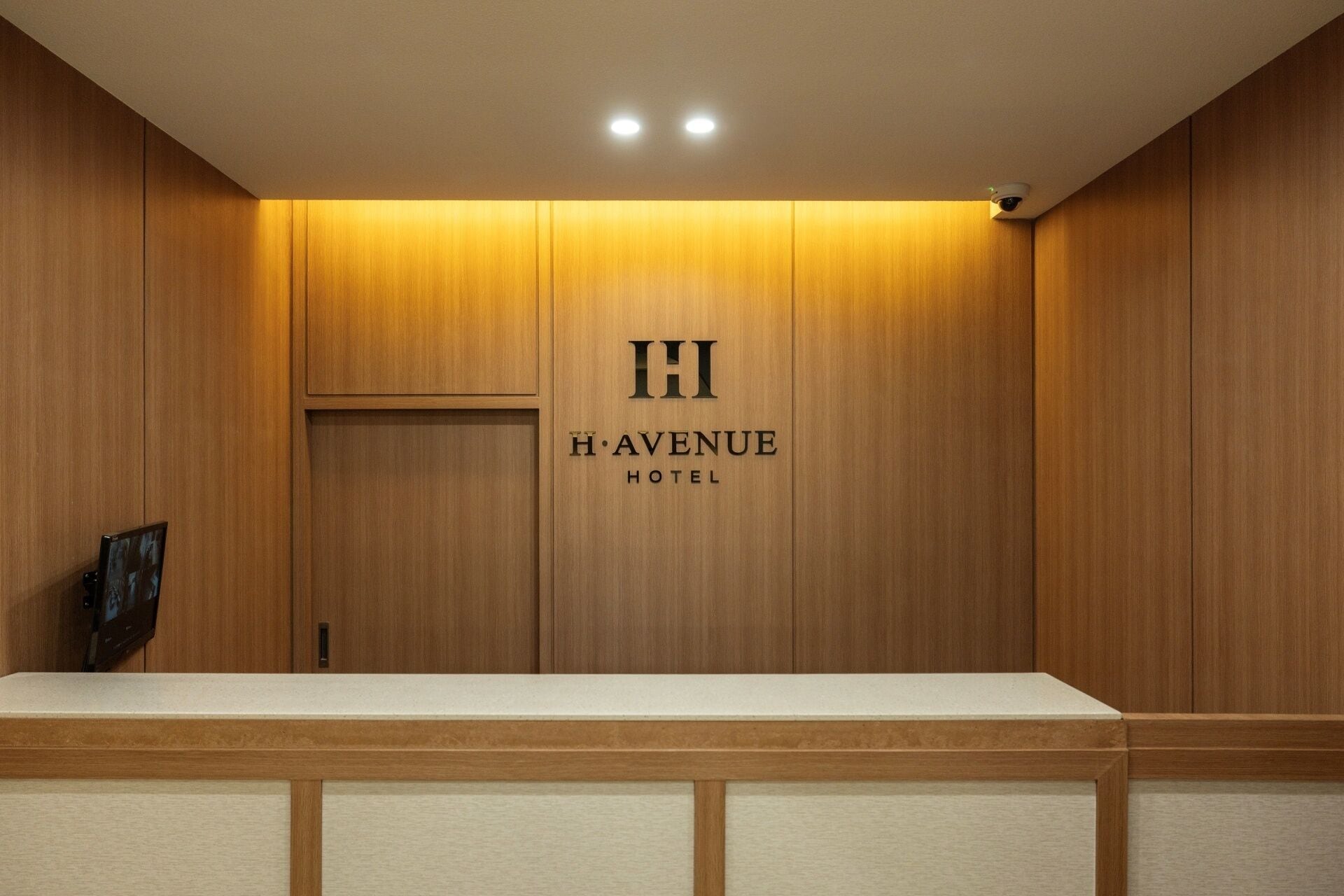 A reception desk with a wooden panel wall and a sign that reads 'H AVENUE HOTEL'.