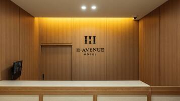 A reception desk with a wooden panel wall and a sign that reads 'H AVENUE HOTEL'.
