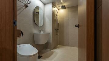 A modern bathroom with a toilet, sink, mirror, and shower.