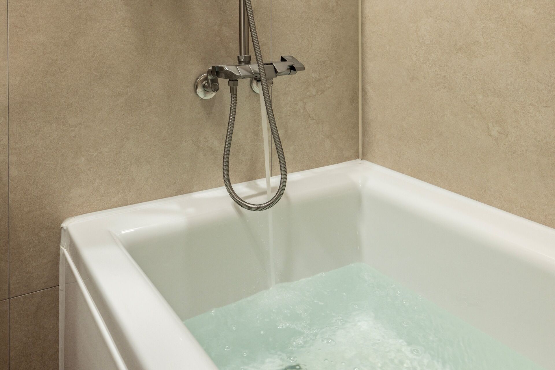 Una bañera blanca con agua corriente, un cabezal de ducha y una manguera flexible.