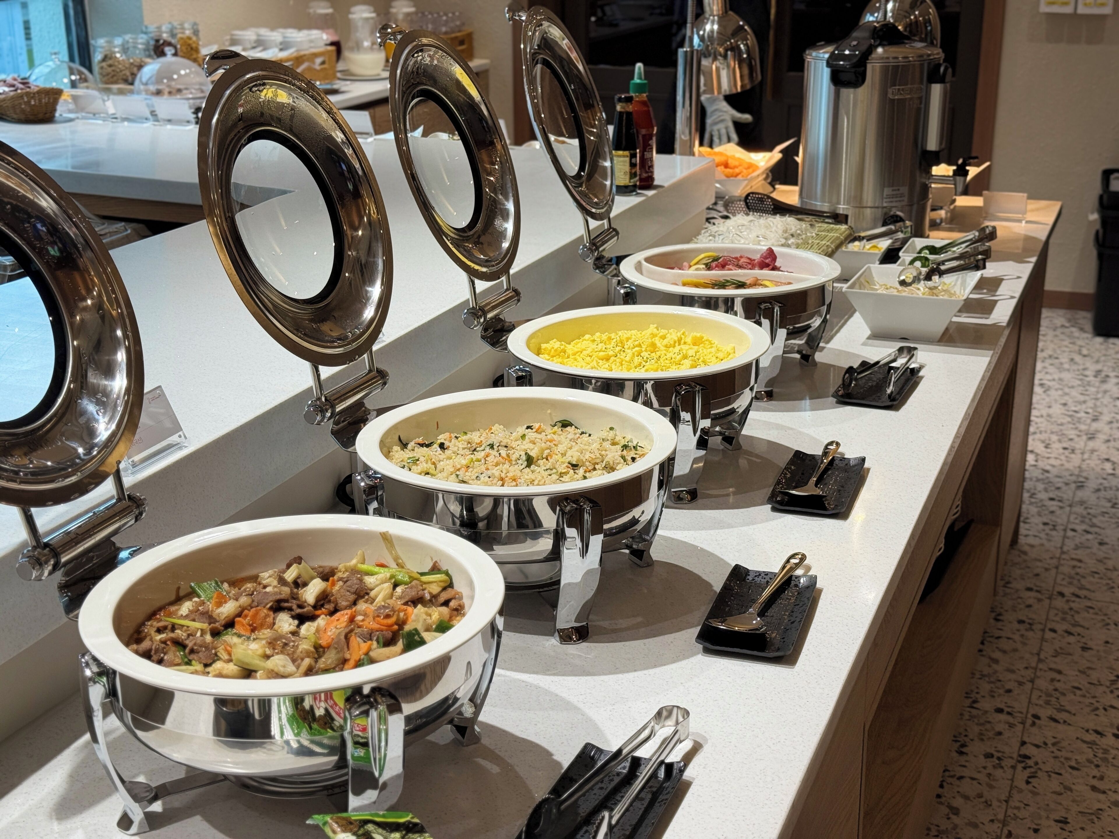 A buffet setup with multiple food stations, each with a lid and serving utensils.