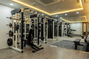 Un gimnasio con diverso equipo de levantamiento de pesas, una banca y un espejo en la pared.