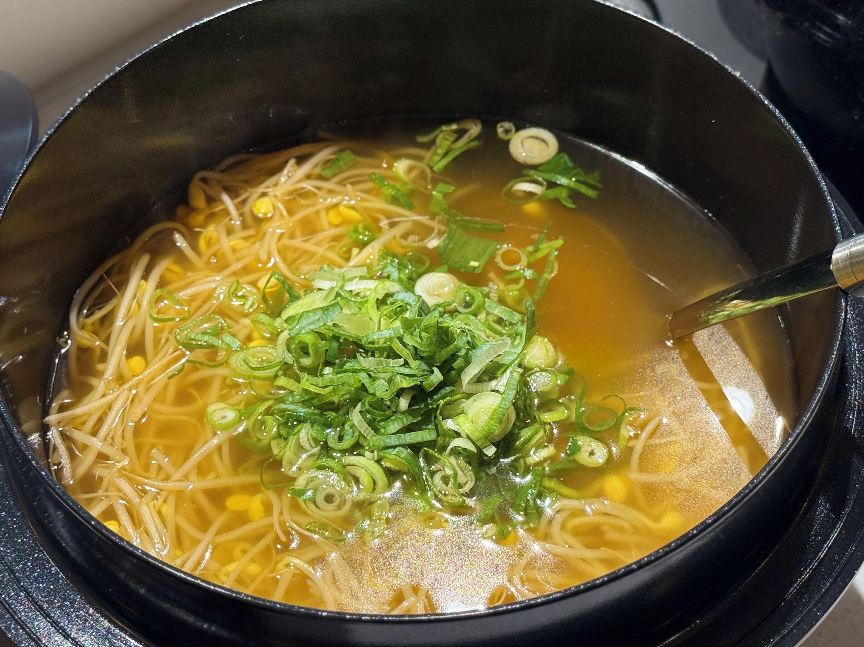 A bowl of noodle soup with corn and green onions.