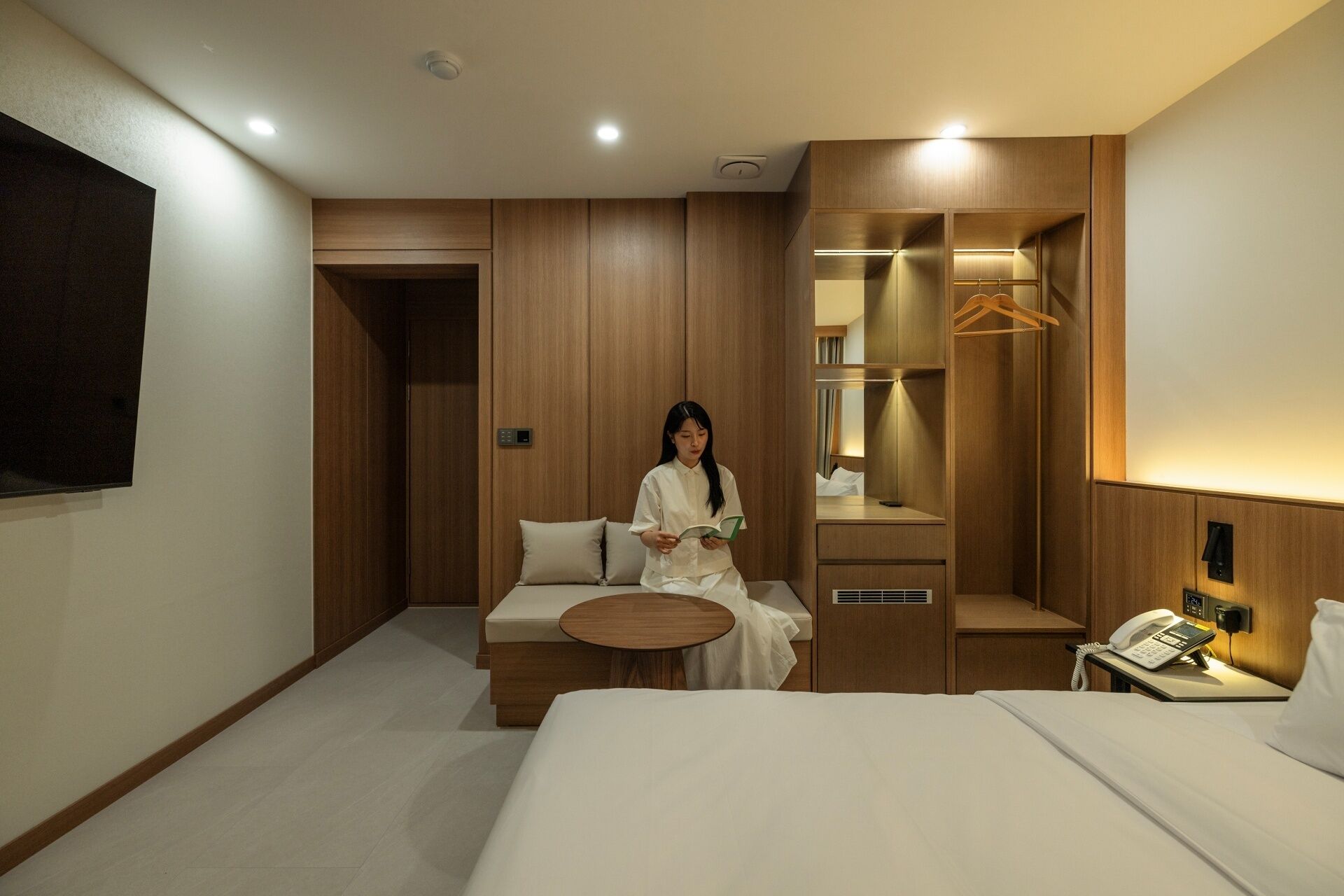 Hotelkamer met een bed, nachtkastje, stoel, rond tafel, garderobe, spiegel, hangkast, telefoon en een tv aan de muur.