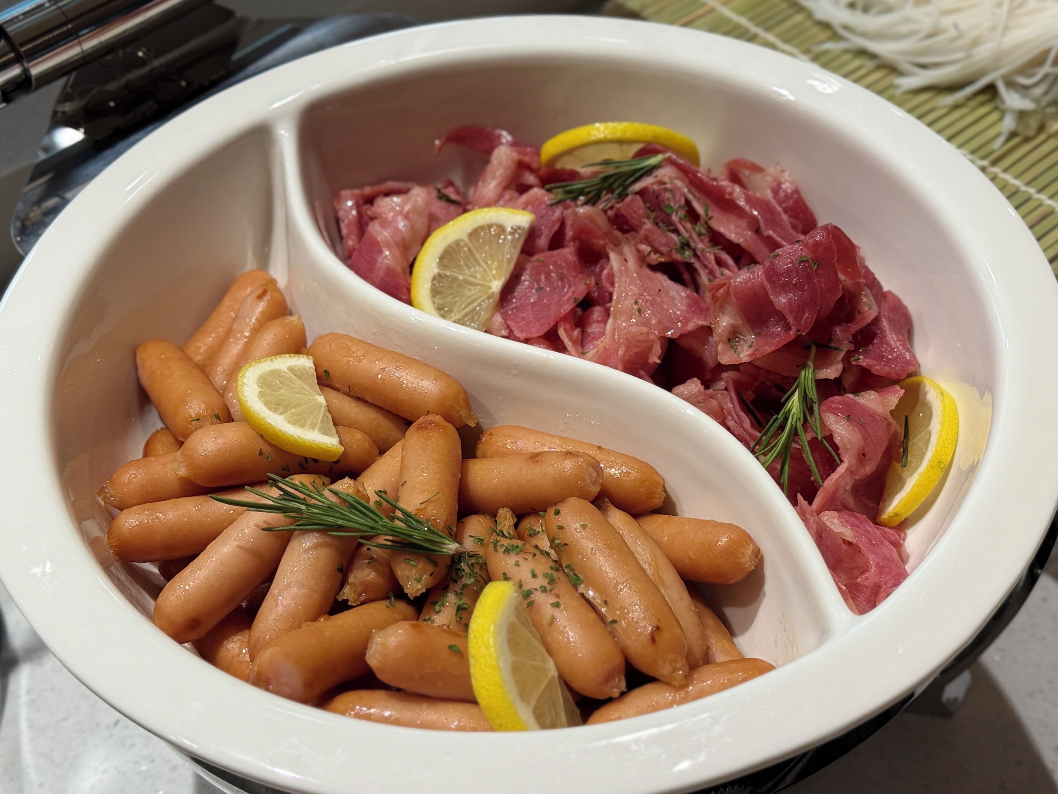 A white ceramic dish containing sliced meat and carrots, garnished with lemon slices and herbs.