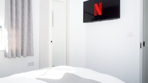 Una camera da letto con un letto, una TV a muro che mostra il logo di Netflix e una porta.