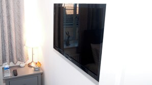 Una stanza con una grande TV a schermo piatto montata a parete, un comodino con una lampada, una bottiglia d'acqua e un telecomando.