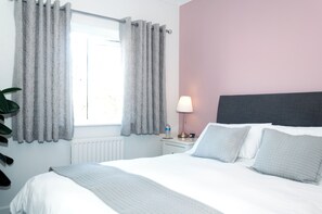 A hotel room with a bed, a nightstand, a lamp, and a window with curtains.