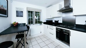 Una cucina moderna con mobili bianchi, un piano di lavoro nero, una cappa in acciaio inossidabile e una finestra che si affaccia sul verde.