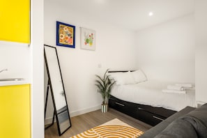 Ein modernes Schlafzimmer mit einem Bett, einem Nachttisch, einem Spiegel und zwei gerahmten Kunstwerken an der Wand.
