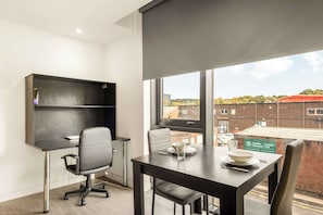 Ein moderner Büroraum mit Schreibtisch, zwei Stühlen, einem Bücherregal und Blick auf Gebäude durch ein großes Fenster.
