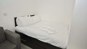 A single bed with white bedding and pillows, a grey armchair, and a black headboard. - Modern & Convenient Studio in Central Sheffield (Sheffield)