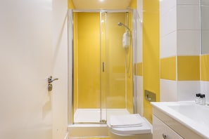 Ein Badezimmer mit einer gläsernen Duschkabine, einem weißen Waschbecken und einer Toilette.