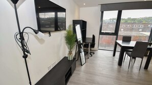 A modern office space with a large window, a desk, chairs, a plant, and a mounted TV. - Modern & Convenient Studio in Central Sheffield (Sheffield)