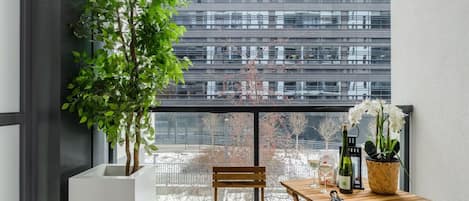 A balcony with a wooden table, a chair, a potted plant, and a view of a modern building.