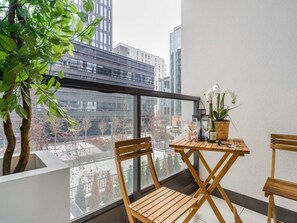Ein Balkon mit Holztisch, zwei Stühlen, einem Blumentopf und einer Weinflasche.