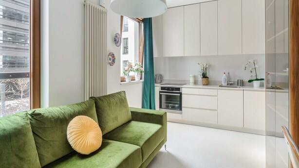 A modern living room with a green sofa, a pendant light, and a view of a kitchen with white cabinets. - Apartment in Porspoder Near Plage du Bourg (Warsaw)
