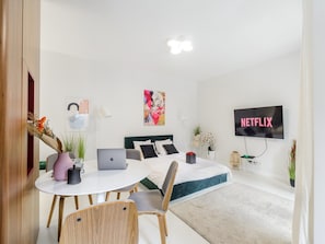 A modern bedroom with a bed, a desk with a laptop, a TV displaying 'NETFLIX', and a round table with chairs. - Convenient Base in Warsaw City Centre (Warsaw)