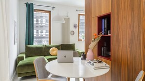 A modern living room with a green sofa, a round white table with a laptop, and a bookshelf with books and decorative items. - Apartment in Porspoder Near Plage du Bourg (Warsaw)