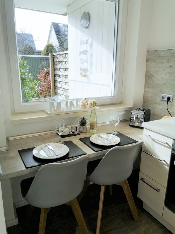 A dining area with a table set for two, a window with a view of the outside, and a kitchen area with a toaster.