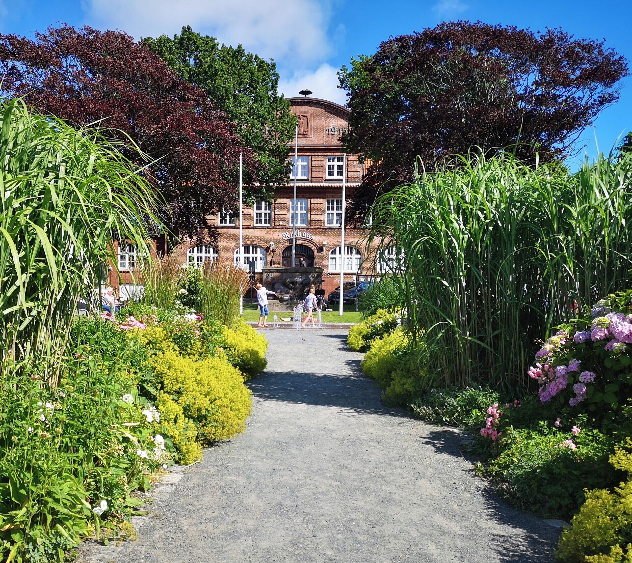 A pathway leading to a brick building with arched windows and a date plaque.